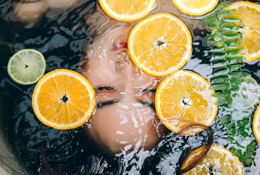 woman's face underwater in bath with fruit slices